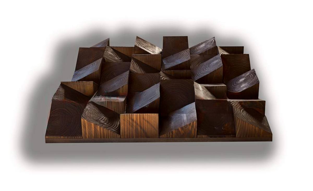 Diffuseur en bois chêne foncé au format horizontal, composé de blocs et de facettes inclinées qui créent un relief géométrique marqué, avec un veinage visible sur la surface sombre.