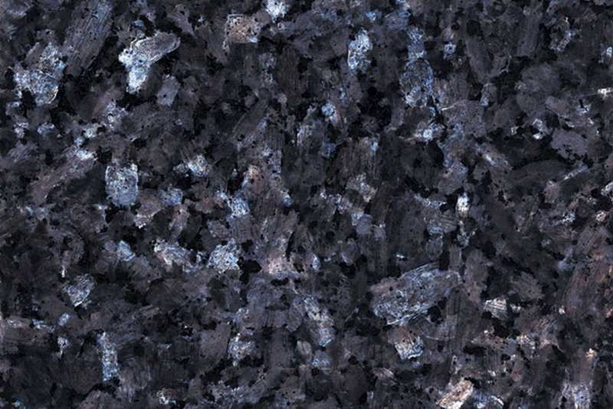 Gros plan sur la texture du granit Blue Pearl, révélant une base sombre ponctuée de grands cristaux aux reflets bleutés et argentés.