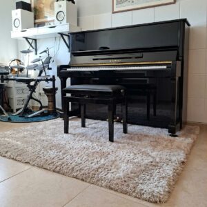 tapis-insonorisant-professional-calm-beige-piano Tapis acoustique beige Professional Calm à poils longs installé sous un piano droit noir dans une pièce de musique, avec une texture épaisse et moelleuse qui apporte confort et améliore l'ambiance sonore.