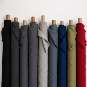 tissu-acoustique-au-metre-collection-de-couleurs Rouleaux de tissu acoustique au mètre alignés dans plusieurs couleurs, notamment noir, gris, gris clair, bleu denim, bleu roi, vert et rouge, avec leur texture textile mate visible.