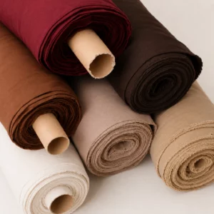 Rouleaux de tissu acoustique au mètre présentés dans des tons bordeaux, brun, taupe, beige et blanc cassé, avec une surface textile fine et des bords de coupe visibles.